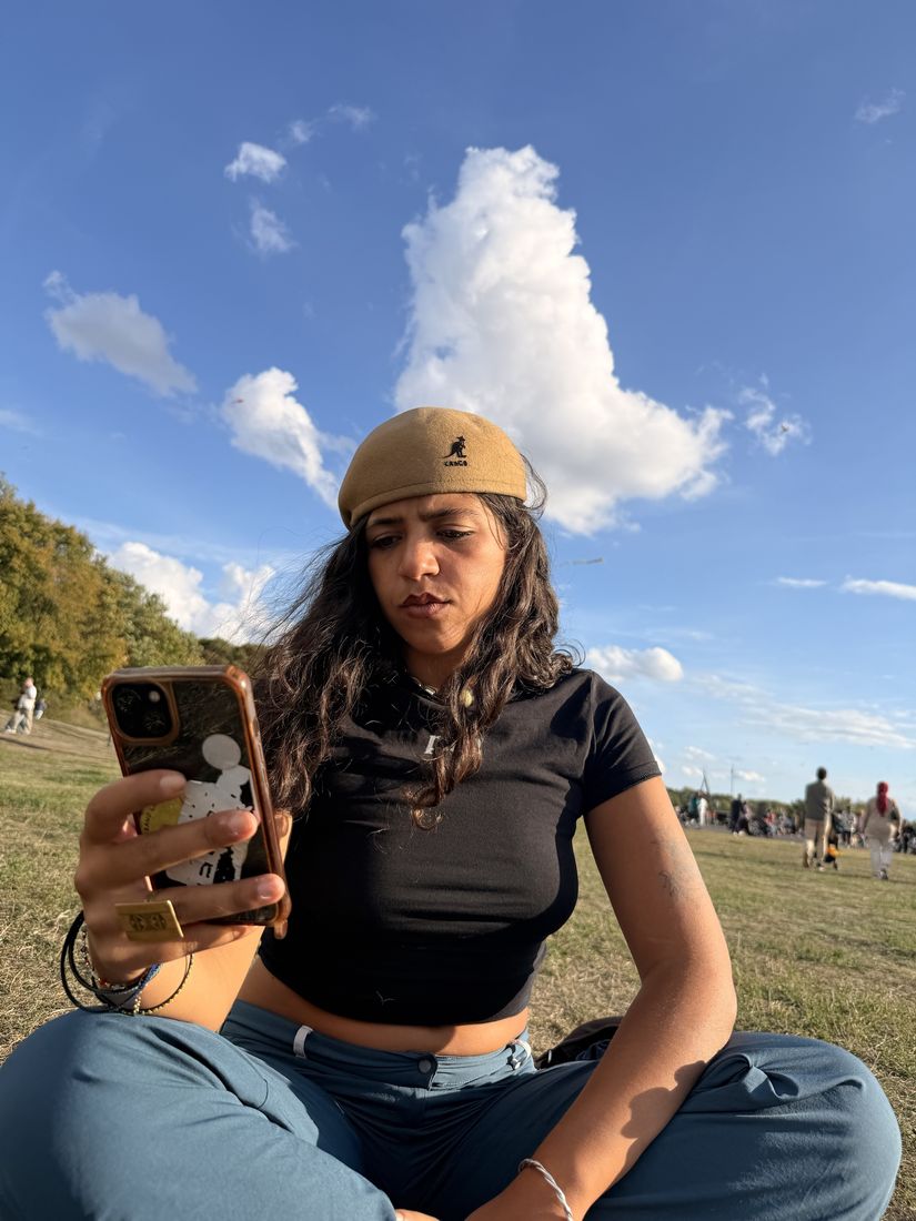 Member in a beige beret sitting on the grass looking at her phone